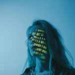 A woman with binary code lights projected on her face, symbolizing technology.