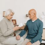 Senior couple measuring blood pressure at home, showcasing care and companionship.