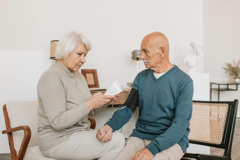 Senior couple measuring blood pressure at home, showcasing care and companionship.
