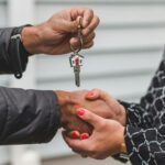 Close-up of a realtor handing over a house key to a new homeowner, symbolizing ownership and investment.